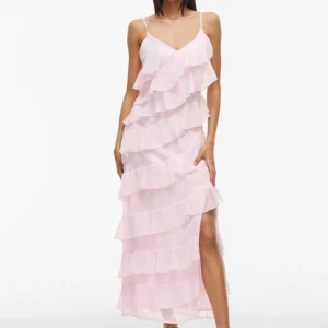 Ljusrosa långklänning med volanger - Superfin ljusrosa långklänning med tunna axelband och flera lager volanger som ger en riktigt drömmig look. Klänningen har v-ringad hals och en slits på sidan för extra edge. Perfekt till bal eller liknande! 