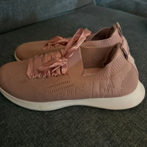 Rosa sneakers med satinsnören - Snygga rosa sneakers från Beez med stickad ovandel och breda satinsnören som ger en cool touch. Skorna har en vit platt sula och rund tå, samt en mjuk och flexibel passform. Perfekta för dig som gillar stilrena och bekväma sneakers med lite extra detaljer.