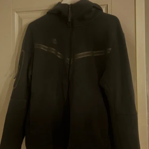 Svart hoodie från Nike med dragkedja - Svart hoodie från Nike med hel dragkedja framtill och huva. Snygga diskreta ränder över bröstet och en ficka med dragkedja på framsidan i storlek L. Tröjan är använd fåtal gånger. Pris går att diskutera vid snabb affär och har möjlighet att skicka samma dag!🫶🏼