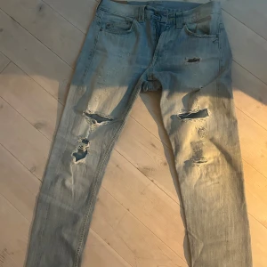 Ljusblå slitna jeans från Dondup - Säljer ett par ljusblå Dondup jeans med snygga slitningar och hål på framsidan. Klassisk femficksmodell med raka ben och normal passform. Jeansen har gul kontrastsöm och Dondup-märke på bakfickan. Perfekt för dig som gillar en avslappnad och trendig look.