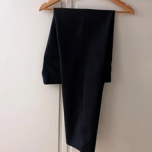 Mörkblå kostymbyxor Tiger of Sweden - Snygga mörkblå kostymbyxor från Tiger of Sweden, modell Tenutas. Klassisk rak passform med bälteshällor och pressveck. Passar bra både till jobb och finare tillställningar. 