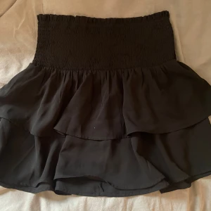 svart volangkjol  - svart kortkjol med stretch i midjan, storlek s men kan passa xs och m. säljer en likadan lila/vit kjol - köp båda för 110 kr