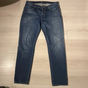 Blå jeans Neuw Stockholm - Snygga blå jeans från Neuw Stockholm med klassisk femficksdesign och kontrastsömmar. Modellen har rak passform och normal midja, tillverkade i slitstarkt denim. Perfekta för dig som gillar stilrena och tidlösa jeans med cool tvätt. 34/34. I princip oanvända 