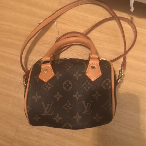 Louis Vuitton monogram handväska - Snygg handväska från Louis Vuitton i klassiskt monogrammönster. Väskan är brun med ljusbruna detaljer och guldiga metalldelar. Den har både handtag och axelrem samt dragkedja upptill. Perfekt storlek för det viktigaste och en riktig statement piece. INTE ÄKTA