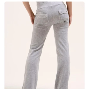 Grå mjukisbyxor med fickor från juicy - Säljer ett par grå mjukisbyxor med bred resår i midjan och praktiska fickor både fram och bak. Byxorna har en rak passform och är tillverkade i mjukt material som är skönt mot huden. Perfekta för chill dagar hemma eller när du vill vara bekväm.