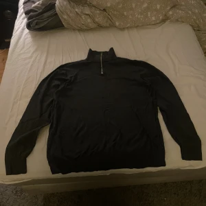 Svart polotröja med half zip - Svart polotröja med halv dragkedja i halsen. Tröjan har långärmade ribbade muddar och är gjord i ett mjukt stickat material. Perfekt för dig som gillar stilren och enkel design med en modern touch.