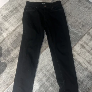 Svarta jeans från Jack & Jones - Svarta jeans från Jack & Jones Jeans Intelligence med klassisk femficksdesign och knappstängning. Jeansen har en rak passform och är tillverkade i mjukt bomullsmaterial med lite stretch för extra komfort. Perfekt för dig som gillar stilrena och enkla svarta jeans.