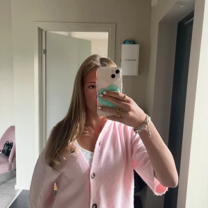 Ljusrosa kofta med knappar - Superfin ljusrosa kofta med svarta knappar framtill. Koftan är mjuk och har en loose passform. Materialet känns fluffigt och stickat, vilket gör den extra mysig. 