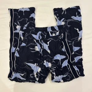 Mönstrade byxor från KappAhl XS - Snygga mörkblå byxor från KappAhl i storlek XS med coolt mönster av ljusblå och vita fåglar. Byxorna har snörning i midjan och vita ränder längs sidorna. 