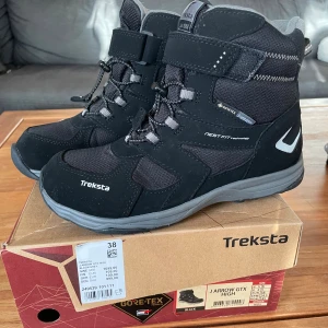 Svarta Treksta J Arrow GTX kängor - Helt nya, oanvända svarta kängor från Treksta, modell J Arrow GTX, med Gore-Tex för vattentäthet och NestFit-teknologi. Inköpspris 1099 kr. Snygg design med snörning, kardborreband och robust mönstrad sula för extra grepp. Materialmix av syntet och skinn, perfekt för höst och vinter. Grå detaljer och rund tå.