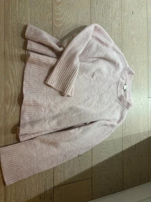 Ljusrosa stickad tröja med ribbade detaljer - Mysig ljusrosa stickad tröja med rund hals och breda ribbade muddar vid ärmslut och nederkant. Tröjan har en loose passform och är perfekt för kyliga dagar. Enkel och stilren design som är lätt att matcha med jeans eller kjol.