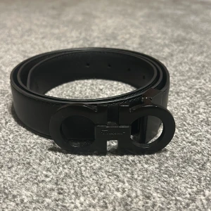 Svart skärp från Salvatore Ferragamo - Säljer ett svart skärp från Salvatore Ferragamo i äkta skinn med ikoniskt Gancini-spänne i svart metall. Bältet har en stilren och klassisk design med slät yta och diskreta sömmar. Perfekt accessoar för att lyfta din outfit. Pris kan diskuteras.