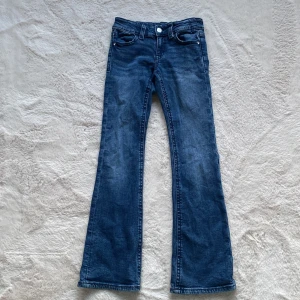 Bootcut jeans med låg midja - Snygga blå jeans med bootcut passform och låg midja. Klassisk femficksmodell med silverfärgade knappar på bakfickorna och dragkedja fram. Jeansen har en lätt tvättad look och är tillverkade i mjukt denimtyg som sitter skönt🩷