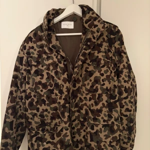 Camouflage parkajacka från Sandro - Parkajacka från Sandro med grymt camouflage-mönster i brunt, beige och grönt. Jackan har flera stora fickor framtill, dragkedja och knappstängning. Perfekt för dig som gillar streetstyle och vill sticka ut med en cool look. (nypris 3800kr) 