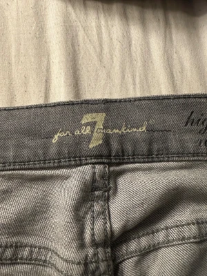 Grå jeans från 7 For All Mankind - Snygga grå jeans från 7 For All Mankind med klassisk femficksdesign och hög midja. Jeansen har raka ben och coola detaljer med silverfärgade nitar på bakfickorna. Perfekt för dig som gillar stilrena och moderna jeans.
