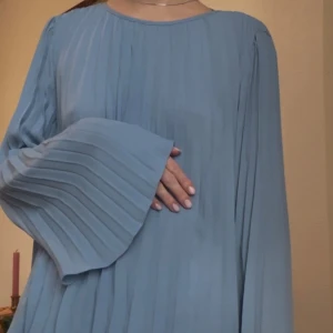 Ljusblå plisserad blus med vida ärmar - Supersnygg ljusblå blus från H&M (storlek S) med plisserat tyg och vida, långa ärmar. Blusen har rund halsringning och ett flowy fall.