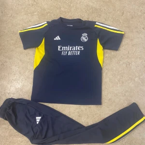 Real Madrid fotbollströja Adidas - Snygg Real Madrid fotbollströja från Adidas i mörkblått med gula och vita detaljer. Tröjan har korta ärmar och tryck med Emirates Fly Better på bröstet samt klubbmärke. Materialet är lätt och andas, perfekt för träning eller match.