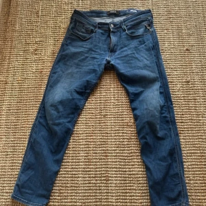 Replay Anbass jeans blå, storlek 34 - Snygga blå Replay Anbass jeans i klassisk femficksmodell med smal passform. Jeansen har en mörk tvätt med lätt slitning och detaljer som dragkedja vid bakfickan. Perfekt för dig som gillar stilrena och moderna jeans. Väljer att sälja dom här jeansen för 349 kr (pris kan diskuteras) Eftersom att dom har ett slaks slithål på ena bak ficka 