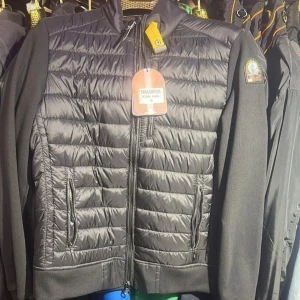 Svart cardigan från Parajumpers - Snygg svart pufferjacka från Parajumpers med quiltad framsida och ärmar i mjuk bomullsmix. Jackan har dragkedja framtill, två fickor med dragkedja och klassisk logga på ärmen. Perfekt för dig som vill ha en stilren och sportig look.