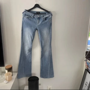 True Religion Joey Low Rise Flare Jeans - Säljer ett par ljusblå True Religion Joey jeans med låg midja och utsvängda ben. Endast använda en gång😊säljs p.ga. för stora för mig