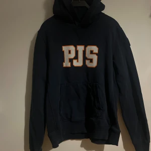 Parajumpers (PJS) hoodie – mörkblå - Snygg och bekväm hoodie från Parajumpers i mörkblå färg med stort PJS-tryck framtill och det klassiska märket på ärmen. Normal passform, mjukt och tjockt material av hög kvalitet. I mycket fint skick!                          KÖPT FÖR 2549 KR PÅ KIDS BRAND STORE!