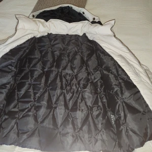 Beige dunjacka från Wolffwear - Snygg beige dunjacka från Wolffwear med quiltat svart foder och dragkedja. Jackan har ribbade muddar, två fickor med knapp och hög krage. Perfekt för kalla dagar och har en klassisk, stilren look.