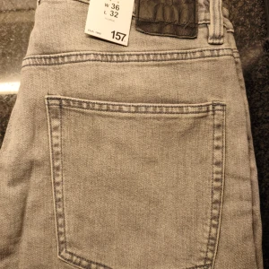Ljusgrå jeansbyxor i rak modell Slimmy - Säljer ett par ljusgrå jeansbyxor i rak passform i modellen Slimmy med klassisk bakficka och snygga kontrastsömmar. Jeansen har bälteshällor och är perfekta för dig som gillar en enkel och stilren look. Passar dig som vill ha en avslappnad vibe. W36 L32