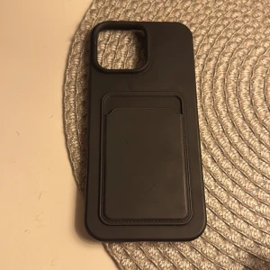 iPhone skal med korthållare - Stilrent svart iPhone-skal med integrerad korthållare på baksidan. Skalet har en stor öppning för kameramodulen och är i gott skick utan synliga repor eller skador. Perfekt för dig som vill skydda din telefon och ha korten nära till hands.
