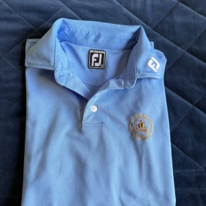 Golfpiké (Lidingö GK) - Snygg ljusblå pikétröja från FootJoy med broderad Lidingö Golfklubb-logga på bröstet. Myxket bra skick, knappt använd.