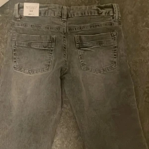 Gråa low waist bootcut jeans Gina Tricot - Snygga grå jeans från Gina Tricot i modellen Scandi low waist bootcut. Jeansen har låg midja, klassiska fem fickor och en lätt tvättad look. Materialet är jeans och passformen är normal med bootcut-snitt. Perfekta för dig som gillar en avslappnad men trendig stil.