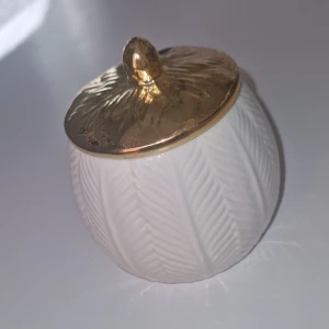 Förvaringsburk - Super fin 'burk/skål' med dekorativt bladmönster och guldfärgat lock. Perfekt för förvaring av småsaker eller som inredningsdetalj. Burken är i fint skick med endast mindre spår av användning-lite små fläckar som jag ej provat att få bort. Elegant och stilren design som passar i de flesta hem.