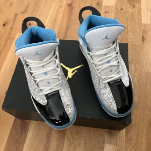 Air Jordan Dub Zero White/University Blue - Air Jordan Dub Zero sneakers i vitt, svart och ljusblått med unikt grafiskt mönster på sidorna. Skorna har snörning, platt sula och detaljer i blankt skinn samt mesh. Insidan är fodrad i blått och tungan har en broderad Jumpman-logga.