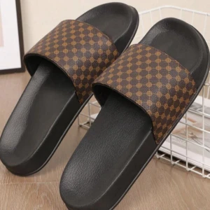 Bruna sandaler med mönster - Svarta sandaler med bred brun rem över foten, dekorerad med ett rutigt mönster i gult. Snygg och enkel design med platt sula, perfekt för sommardagar. Remmen är i syntetmaterial och sulan är mjuk och bekväm.