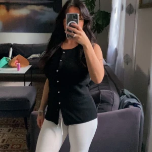 Svart ärmlös blus med knappar S - Svart blus med rund hals och ärmlös design. Toppen har silverfärgade knappar framtill och en lätt figurnära passform. Materialet ser ut att vara mjukt och bekvämt, perfekt för att styla med jeans eller kjol. Snygg och enkel att matcha med olika accessoarer.