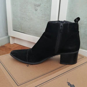 Svarta mocka stövletter  Vox Shoes strl 40 - Coola ankel stövletter från Voi Shoes i mocka med spetsig tå och låg klack. Skorna har dragkedja i guld på sidan.Perfekta för dig som gillar klassiska boots med lite edge. Det står 41, men är som en 40, därvad jag behöver sälja dom. Mycket lite använd.