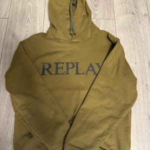 Olivgrön hoodie från Replay - Säljer en olivgrön hoodie från Replay med stor logga framtill. Tröjan har huva med snörning och är tillverkad i mjuk bomull. Perfekt för dig som gillar en clean och avslappnad stil.