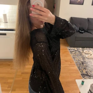 Svart paljettblus från Urban Classics - Säljer en svart blus från Urban Classics med glittriga paljetter över hela toppen. Blusen är långärmad och har en lätt transparent mesh-look som ger en edgy vibe. Perfekt för dig som vill sticka ut med lite extra bling. Storlek L.