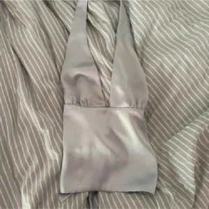 Blå halterneck topp - Säljer en blå halterneck topp i glansigt satinliknande material. Toppen har djup v-ringning och knytning i ryggen för en snygg omlott-effekt. Perfekt för dig som vill sticka ut med en stilren och trendig look. Priset är diskuterbart 💗