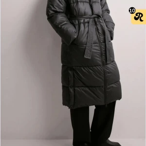 Svart lång pufferjacka med bälte - Säljer en svart lång pufferjacka med bälte i midjan och dragkedja framtill. Jackan har en quiltad design och är perfekt för kalla dagar. Den har långa ärmar och en oversized passform. Köpte den för 999kr och säljer den för 600kr. Priset kan diskuteras vid snabbaffär