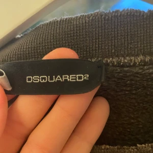 Svart crewneck från Dsquared2 - Säljer en svart crewneck från Dsquared2 med vit text 'RANGER' och lönnlöv på bröstet. Tröjan har rund halsringning och långa ärma.. Perfekt för dig som gillar streetwear och vill ha något från ett exklusivt märke. Har en sliten look!