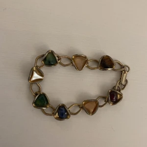 Färgglatt armband med stenar i guldton - Unikt armband i guldton med triangulära stenar i grönt, blått, vitt, brunt och rött. Vet ej om det är riktigt guld, stenar är riktiga.