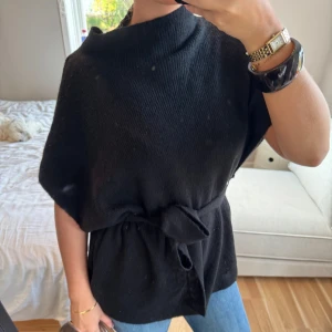 Svart stickad tröja med knyt i midjan❣️ - Säljer en svart stickad tröja med hög krage och korta ärmar. Tröjan har ett snyggt knytband i midjan som ger en fin siluett. Perfekt att styla med jeans eller kjol för en chill och trendig look.