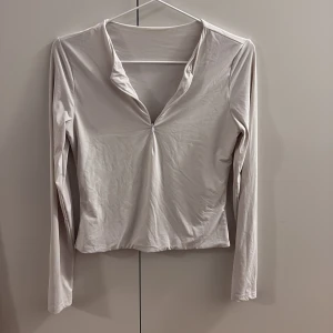 Tränings tröja - Säljer en stilren vit långärmad topp med v-ringning framtill. Toppen har en mjuk och slät yta, perfekt för dig som gillar minimalistisk stil. Passar dig som vill ha en enkel men snygg look. Tränings material 