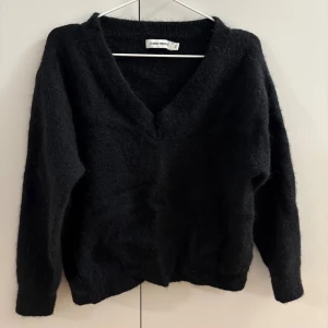 Svart stickad tröja CW - Mysig svart stickad tröja från CW med v-ringad hals och lång ärm. Perfekt för lager-på-lager och chill dagar. Enkel att matcha med jeans eller kjol för en clean look.