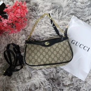 Fint axelväska med kedja - Snygg axelväska mönster i beige och svart. Väskan har guldfärgad kedja, svarta skinn-detaljer och dragkedja upptill. Perfekt storlek för det viktigaste och ger en lyxig touch till din outfit.