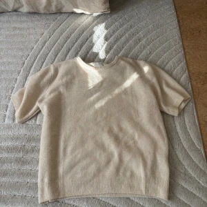 Beige stickad kortärmad tröja - Superfin beige stickad tröja med korta ärmar och rund hals. Tröjan har ribbade kanter vid ärmslut och nederkant, vilket ger en clean och stilren look. Perfekt att styla med jeans eller kjol för en chill vibe.