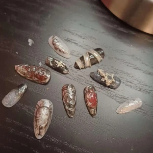 Svarta och röda dekorerade lösnaglar - Unika lösnaglar i svart, rött och silver med 3D-mönster och detaljer som stjärnor och pärlor. Naglarna har en glansig finish och olika former, vissa spetsiga och andra mer rundade. Perfekt för dig som vill ha ett statement på händerna.