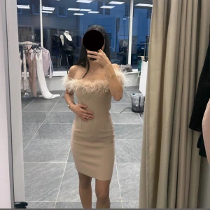 Kort rosa klänning med fjädrar - Säljer en superfin beige offshoulder klänning med tight passform och fjäderdetaljer längs urringningen. Klänningen är kort och har en stilren, elegant look som verkligen sticker ut. Finns i alla storlekar XS-XL.                                                      Pris går att diskutera.