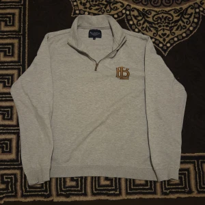 Grå half zip tröja från Bondelid XL/L - Snygg ljusgrå tröja från Bondelid i storlek XL/L med brunt broderat BL-logga på bröstet. Tröjan har half zip-dragkedja, hög krage och är långärmad. Perfekt för lager-på-lager och chill stil. Pris kan diskuteras