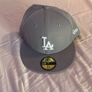 Grå LA-keps  - Säljer en grå New Era 59FIFTY keps med LA-logga broderad framtill i vitt. Klassisk flat peak och broderad New Era-logga på sidan. Har aldrig använts då jag råkade beställa en för stor.  kommer med hatstore stickers och låda. Nypris:499 mitt pris :409